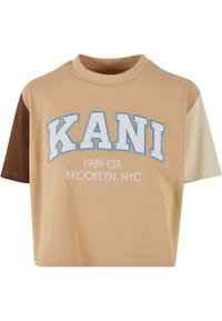 Trumpa, trumpomis rankovėmisT-marškiniai, pagaminti iš béžinės ir rudos medvilnės. Su šviesiai mėlyna ir balta siuvinėjimu užrašais "KANI" ir "BROOKLYN, NYC".