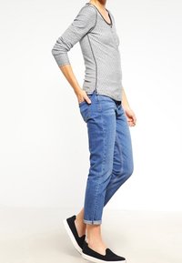 Grey patterned long-sleeve shirt with black trim, paired with blue rolled-up jeans and black slip-on shoes, showcasing a casual fit.