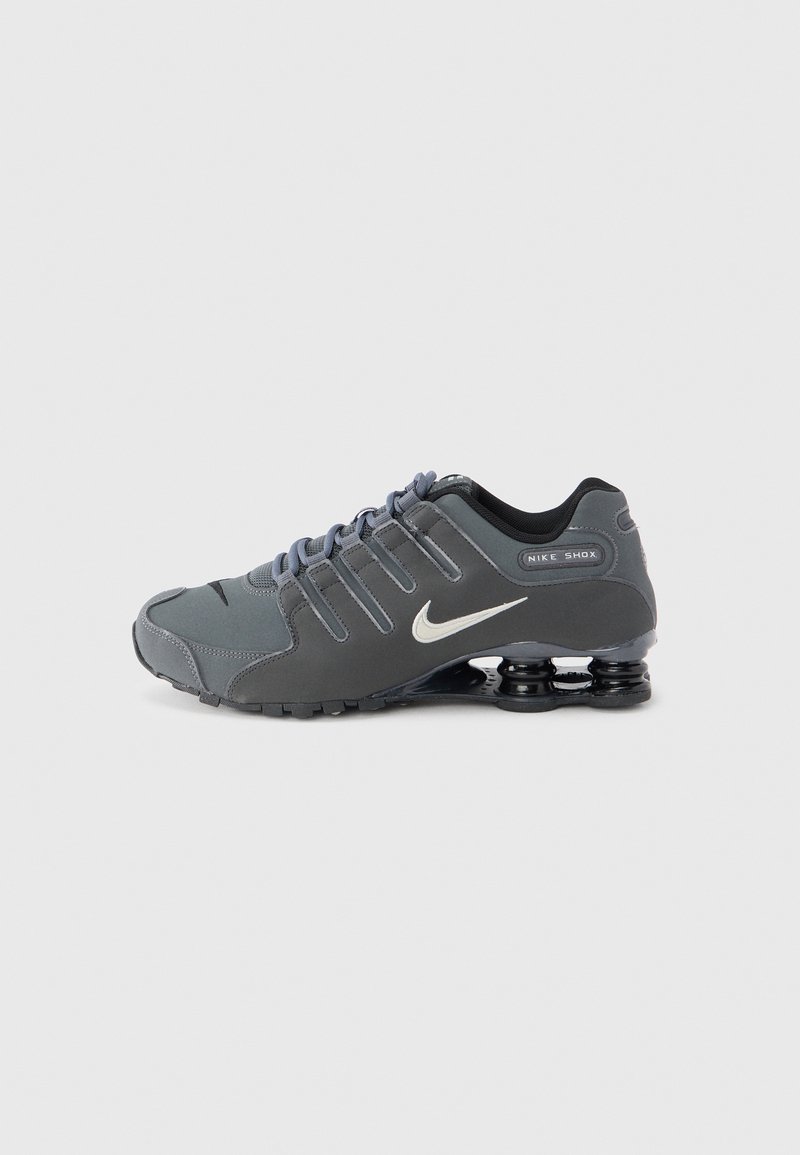 Nike Shox sneakers in dark gray with a sleek design. Features include mesh panels, textured accents, and a distinctive black shock-absorbing sole.