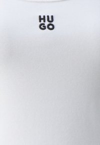 White cotton t-shirt featuring a ribbed texture and a black embroidered logo "HUGO" centered on the chest.
