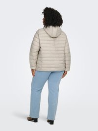Light beige puffer jacket with a hood, featuring horizontal quilted pattern, elastic cuffs, and a relaxed fit, paired with light blue jeans.