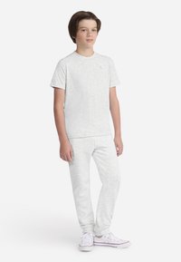 T-shirt gris clair en coton à manches courtes avec col rond, assorti à un pantalon de la même couleur. Les deux ont une texture douce et une coupe décontractée, portés avec des baskets blanches.