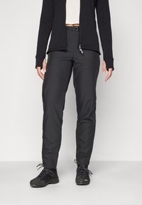 Svart teknisk bukse med slim fit, med sidelommer, teksturert stoff og en sikker beltesløyfe. Kombinert med tursko.