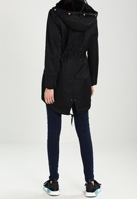 Svart parka-jacka med foder i päls, åtdragen midja och dragsko i fållen. Parat med mörka jeans och svarta sneakers med blå detaljer.