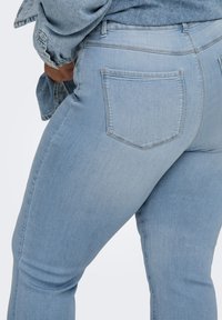 Άτομο που φοράει ανοιχτό μπλε τζιν παντελόνι και τζιν μπουφάν που ταιριάζουν, με το ένα χέρι να διορθώνει το μπουφάν στη μέση.