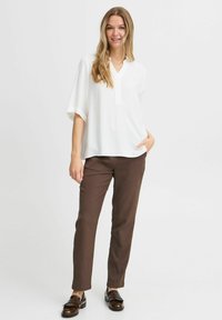 Bílá, strukturovaná, krátkosrstá košile s výstřihem do V, spárovaná s hnědými, slim-fit kalhotami a černými mokasíny s třásněmi.