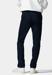 Jeans bleu foncé à coupe slim, en denim. Poches arrière visibles et matériel minimal. Associés à des sneakers blanches.