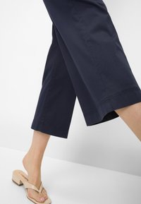 Navy Cropped-Hosen mit gerader Schnittführung und Saumdetails, kombiniert mit beigen Flip-Flop-Sandalen mit einem dicken Riemen und leichtem Absatz.