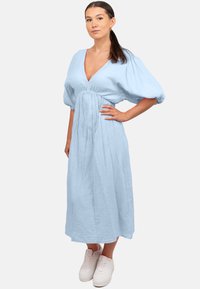 Robe midi bleu clair en tissu texturé, dotée d'un décolleté plongeant, de manches bouffantes et d'une taille froncée, associée à des baskets blanches.