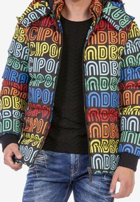 Kleurrijke pufferjas met een zwarte achtergrond, voorzien van gedurfde, meerkleurige tekstpatronen. Inclusief capuchon en ritssluiting aan de voorkant.