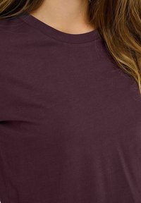 T-shirt bordeaux a maniche corte in morbido cotone, con scollatura rotonda e texture liscia, caratterizzato da dettagli di cucitura minimi.