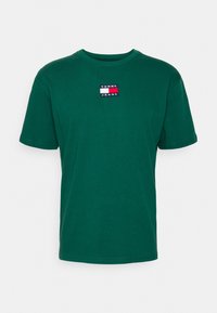 Grön bomullströja med korta ärmar, rund halsringning och en rektangulär broderad logotyp i röd, vit och blå på bröstet.