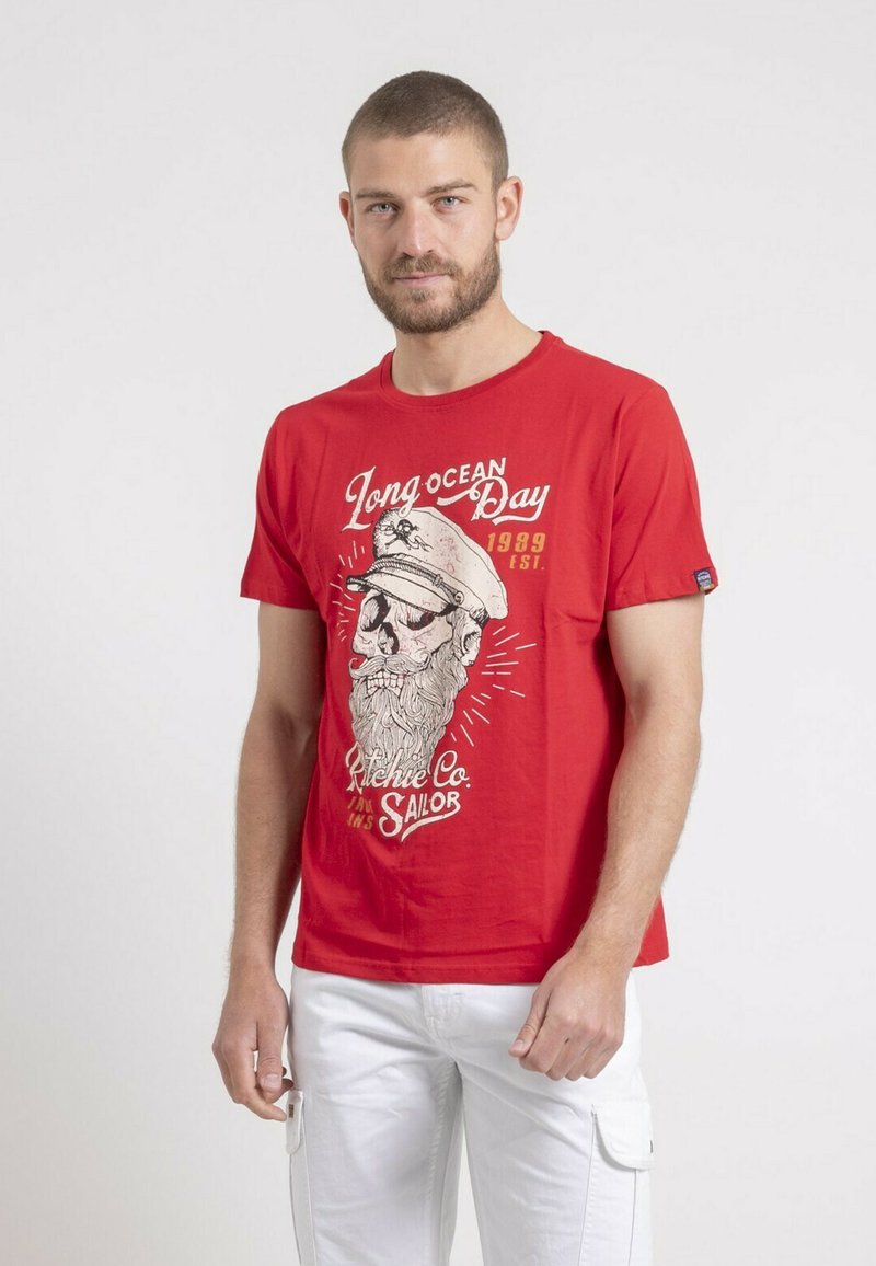 T-shirt en coton rouge avec un imprimé graphique d'un crâne portant un chapeau de marin et une barbe, avec le texte "Long Ocean Day" en blanc et noir.