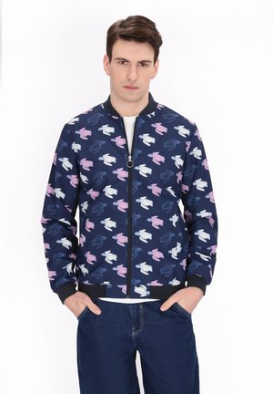 Marine bomberjack met een gedrukt patroon van schildpadden in roze, wit en blauw. Bevat een rits aan de voorkant en ribgebreide manchetten en zoom.