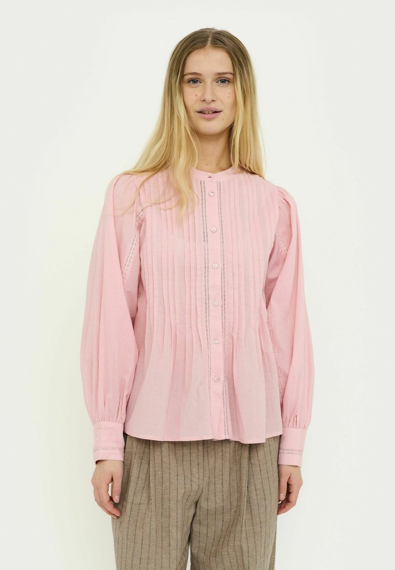 Ružová blúzka na gombíky s riasením, okrúhlym golierom a dlhými nafúknutými rukávmi. Ľahká tkanina s jemnými švami. Kombinovaná s béžovými pruhovanými nohavicami.