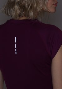 Bordeaux atletisk t-shirt med korta ärmar, med ett vitt vertikalt bälte på ryggen för synlighet. Texturerad tyg med en tajt design.
