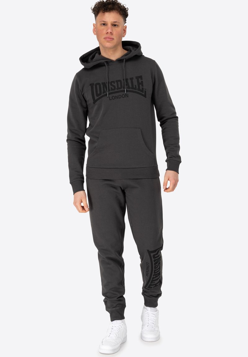 Grå hoodie og joggers sæt lavet af bomuldsblanding. Har en frontlomme, ribbede manchetter og logo print i sort på sweatshirt og bukser.