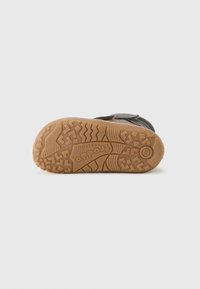Brown rubber outsole with textured grips, featuring a distinctive tread pattern and embossed logo. Gray upper with velcro strap detail.