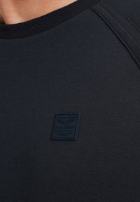 Marineblauwe crewneck hoodie gemaakt van zachte stof, met een gestructureerde logopatch op de linkerkant van de borst en ribgebreide kraag en naden.