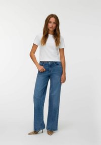 Bela skrajšana majica, modri široki jeans z visokim pasom in mule z vzorcem kače; gladka tekstura s klasičnim dizajnom jeansov.
