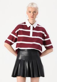 Πολυεστερικό πουκάμισο με μπορντώ και λευκές ρίγες και λευκό γιακά, συνδυασμένο με μαύρη πλισέ φούστα από τεχνητό δέρμα. Υφή υφάσματος και άνετη εφαρμογή.