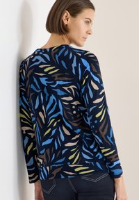 Długi rękaw, granatowa baza z abstrakcyjnymi wzorami w odcieniach niebieskiego, zielonego i brązowego. Miękka tkanina, luźny krój z zaokrąglonym dołem.