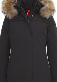 Parka nera con cappuccio foderato in pelliccia, chiusura con zip, due tasche laterali e dettagli di cucitura discreti. La pelliccia è di un marrone chiaro e ha una consistenza morbida.