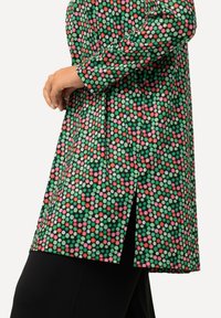Tunic verde con un motivo di pois colorati in rosso, rosa e bianco. Presenta uno spacco laterale e maniche lunghe, realizzata in tessuto morbido.