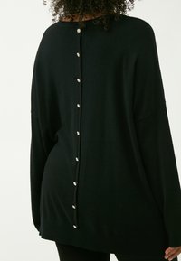 Schwarzer, oversized Pullover mit Rundhalsausschnitt und dekorativen Knopfdetails, die entlang des Rückens verlaufen. Hergestellt aus weichem, strukturiertem Stoff.