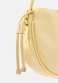 Gelbe Ledertasche mit glänzenden silbernen Nieten, geschwungener Form und weicher Textur. Verfügt über zwei Kordelzüge mit metallischen Akzenten.