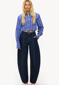 Camisa azul a rayas recortada con mangas largas combinada con pantalones vaqueros oscuros de talle alto, con costuras laterales y corte holgado.