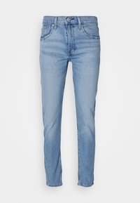 Ljusblå slim-fit jeans med fem fickor, knäppning med knapp och bälteshällor, visade på en enkel vit bakgrund.