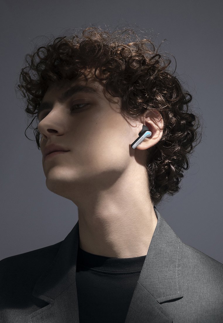 Cuffie wireless con un design bianco e blu, caratterizzate da una forma elegante. L'utente ha i capelli ricci e indossa un blazer grigio.