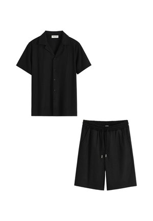 Chemise noire à manches courtes avec boutons et col, associée à un short noir à taille élastique avec cordon, sur fond blanc.