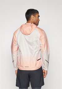 Lett jakke med gradientdesign fra lys rosa til hvit, med glidelåslommer og hette. Stoffet ser jevnt og pustende ut.