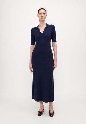 Navy Midi-Kleid aus Strick mit kurzen Ärmeln, V-Ausschnitt, gerippter Textur und seitlichen Schlitzen, kombiniert mit glänzenden burgunderfarbenen Ballerinas.