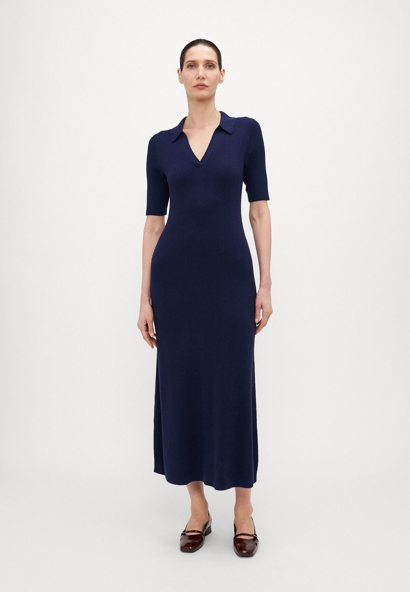 Robe midi en tricot navy avec des manches courtes, décolleté en V, texture côtelée et fentes sur les côtés, accompagnée de ballerines bordeaux brillantes.