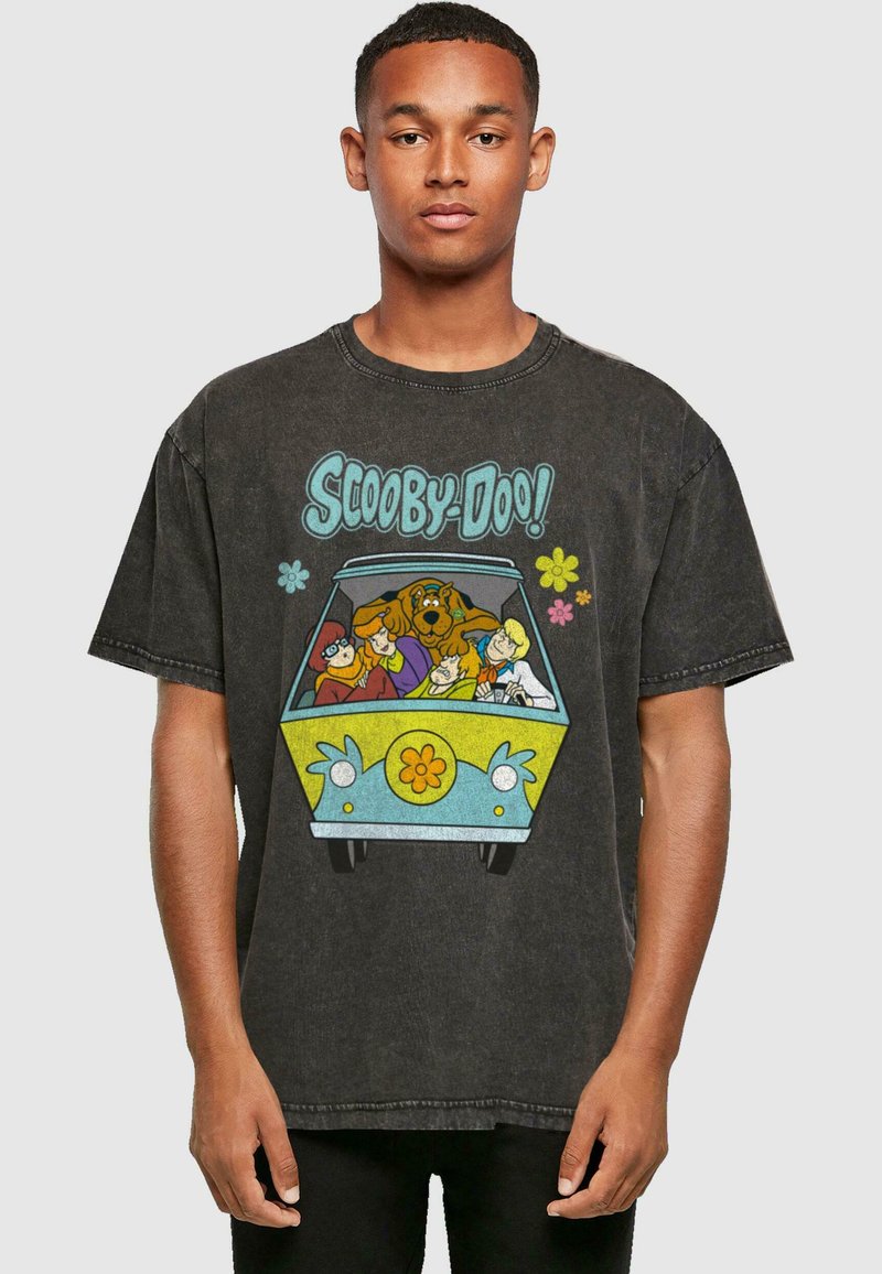 Camiseta negra de gran tamaño con un gráfico colorido de Scooby-Doo que muestra a los personajes en una furgoneta, con acentos en azul claro y amarillo, y detalles florales.