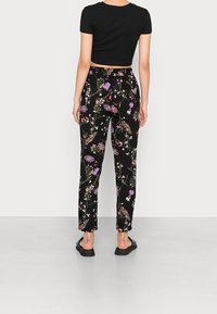 Svarta blommiga byxor med lös passform, prydda med ett färgglatt blommönster, kombinerade med en kort svart topp och platta svarta sandaler.