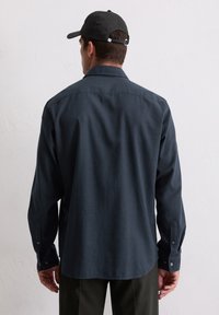 Donkerblauwe, lange mouwen blouse met een gestructureerd ruitpatroon. Voorzien van een klassieke kraag en knopenmanchetten.