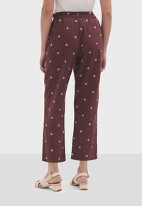 Pantalons bordeaux texturés à coupe ample, dotés d'un motif à rayures verticales et de losanges géométriques de couleur crème, avec une taille élastique et une longueur cropped.