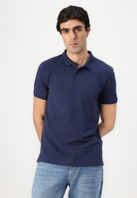 Jūrinės mėlynos spalvos polo marškiniai su trumpomis rankovėmis, turintys klasikinį apykaklę ir subtilų logotipą. Medvilnės mišinio audinys, glotni tekstūra ir prigludusi forma.