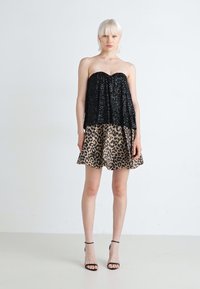 Top senza spalline di paillettes nere con gonna a campana in stampa leopardata. L'outfit presenta una combinazione di texture e un design al ginocchio.