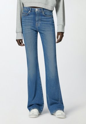 Jeans in denim blu a gamba larga con vita alta, dotati di chiusura a bottone e design a cinque tasche; indossati con un pullover corto grigio chiaro.