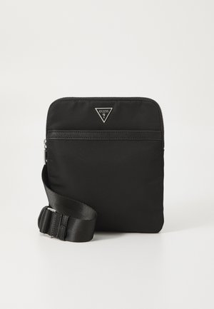 Sac bandoulière noir en nylon avec sangle réglable, fermeture à glissière, poche avant et emblème en logo ton argent. Forme rectangulaire plate, texture lisse.