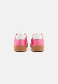 Zapatillas sintéticas rosas con acentos blancos y una suela de goma marrón. La vista trasera muestra una textura suave y un diseño de cordones.