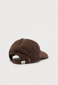 Brūns korduroja cepure ar ribotu tekstūru, izliekts vizieris un regulējama siksna aizmugurē ar metālisku akcentu.