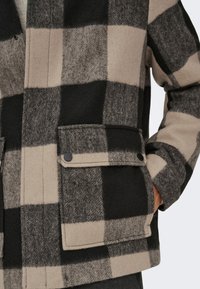 Svart, grå och beige rutig kappa i texturerad ull med fickor med knappar och krage.