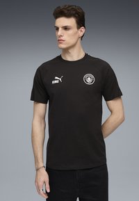 Sort t-shirt lavet af bomuld, med rund hals, korte ærmer og Manchester City-logo. Udsmykket med hvid Puma-branding.