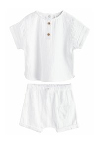 Conjunto de dos piezas de algodón blanco que consiste en una blusa de manga corta con tapeta de botones y pantalones cortos a juego con cintura elástica y bolsillo.